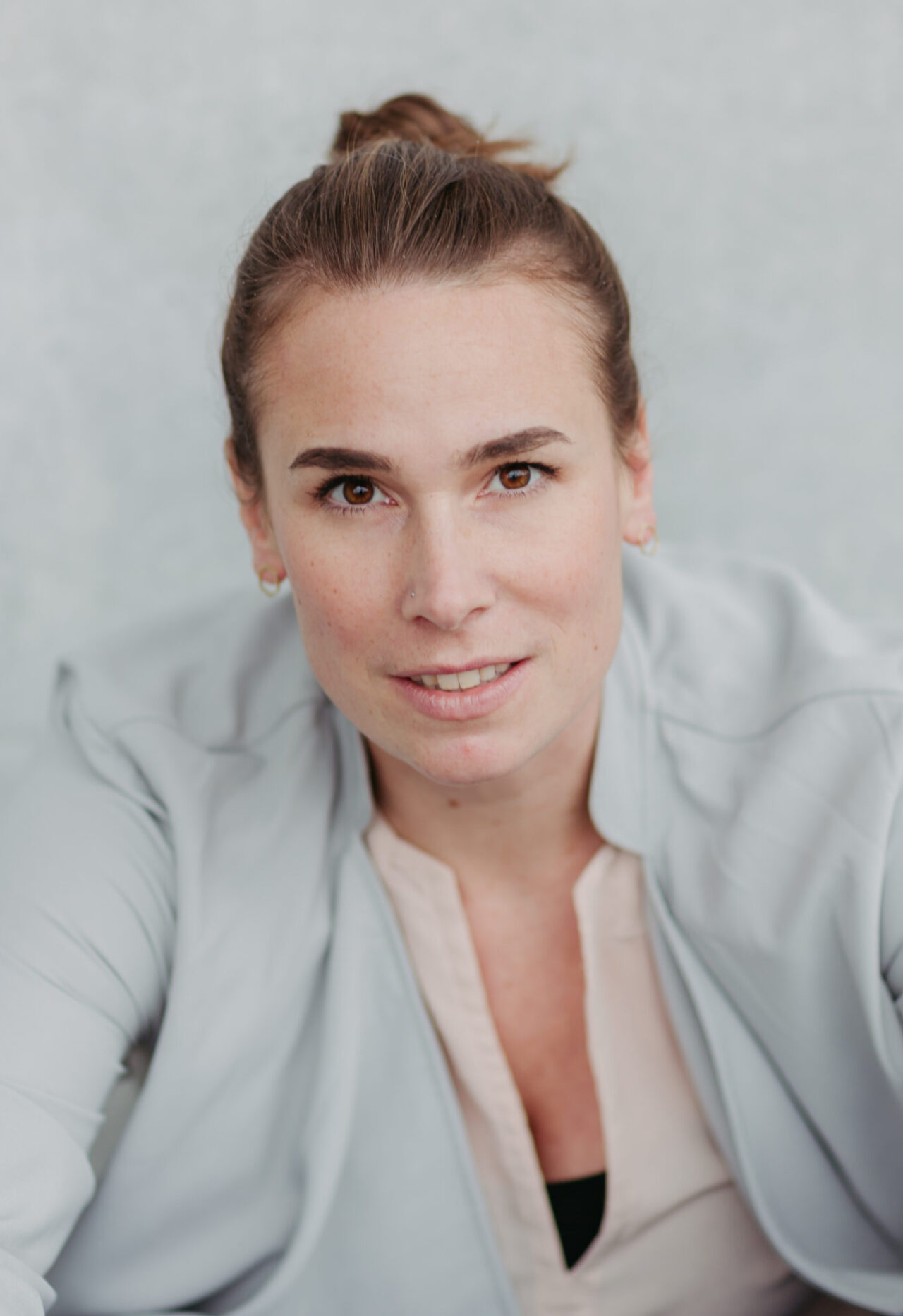 Frau mit hochgesteckten Haaren blickt frontal in die Kamera und sitzt vor einer hellen Wand.