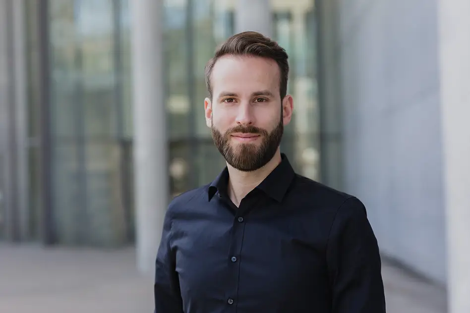 Business Portrait eines Mannes mit Bart in schwarzem Hemd vor moderner Glasarchitektur, Personal Branding Fotografie